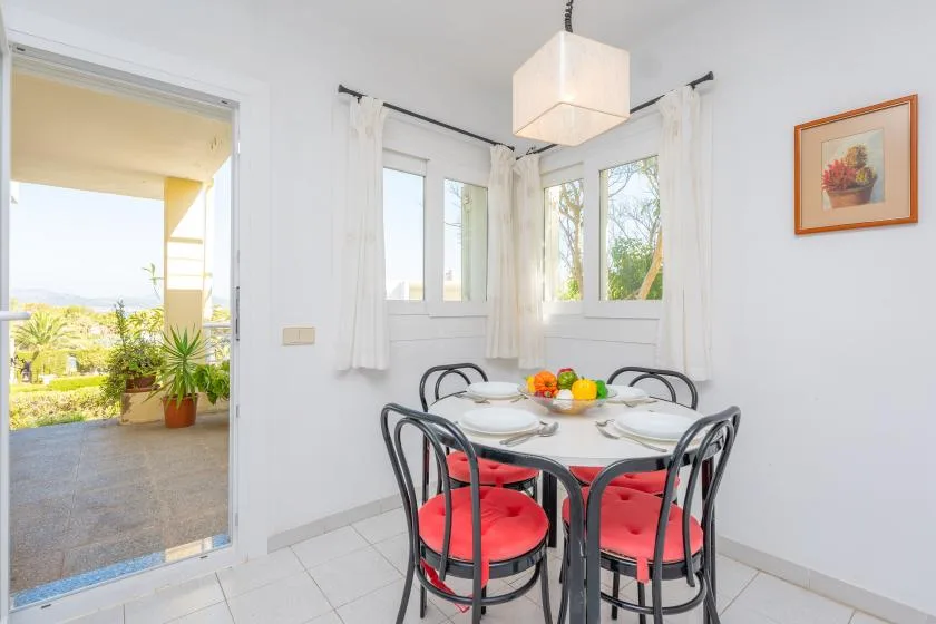 A bright dining area with a round table and red-cushioned seating beside large windows.