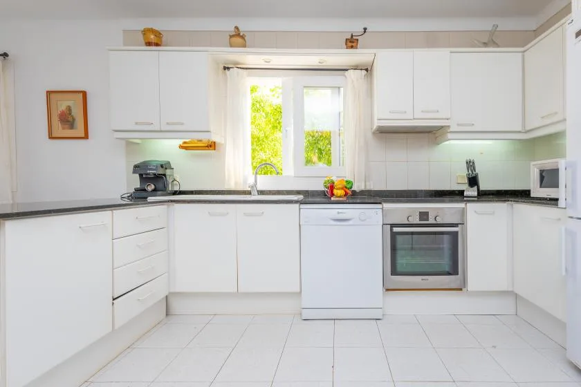A bright white kitchen with cabinets, a window, and built-in appliances.