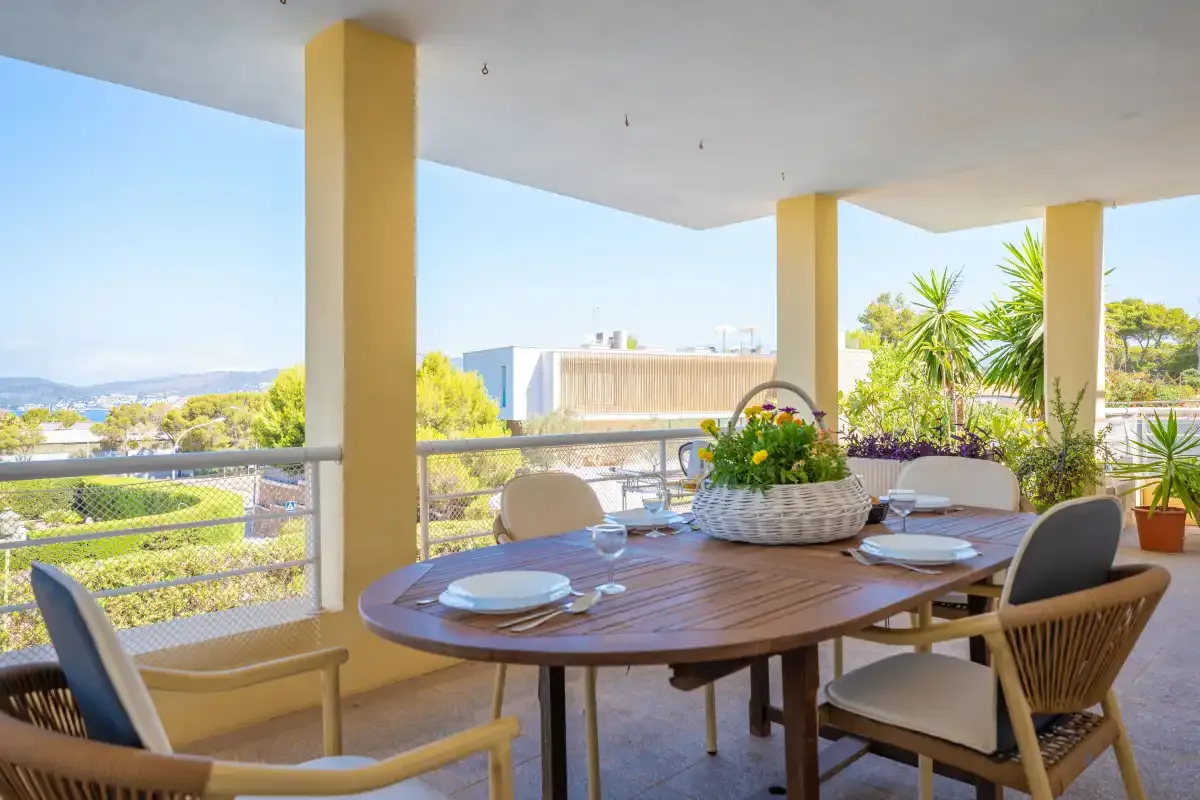 A covered outdoor dining area with a set table and garden views.