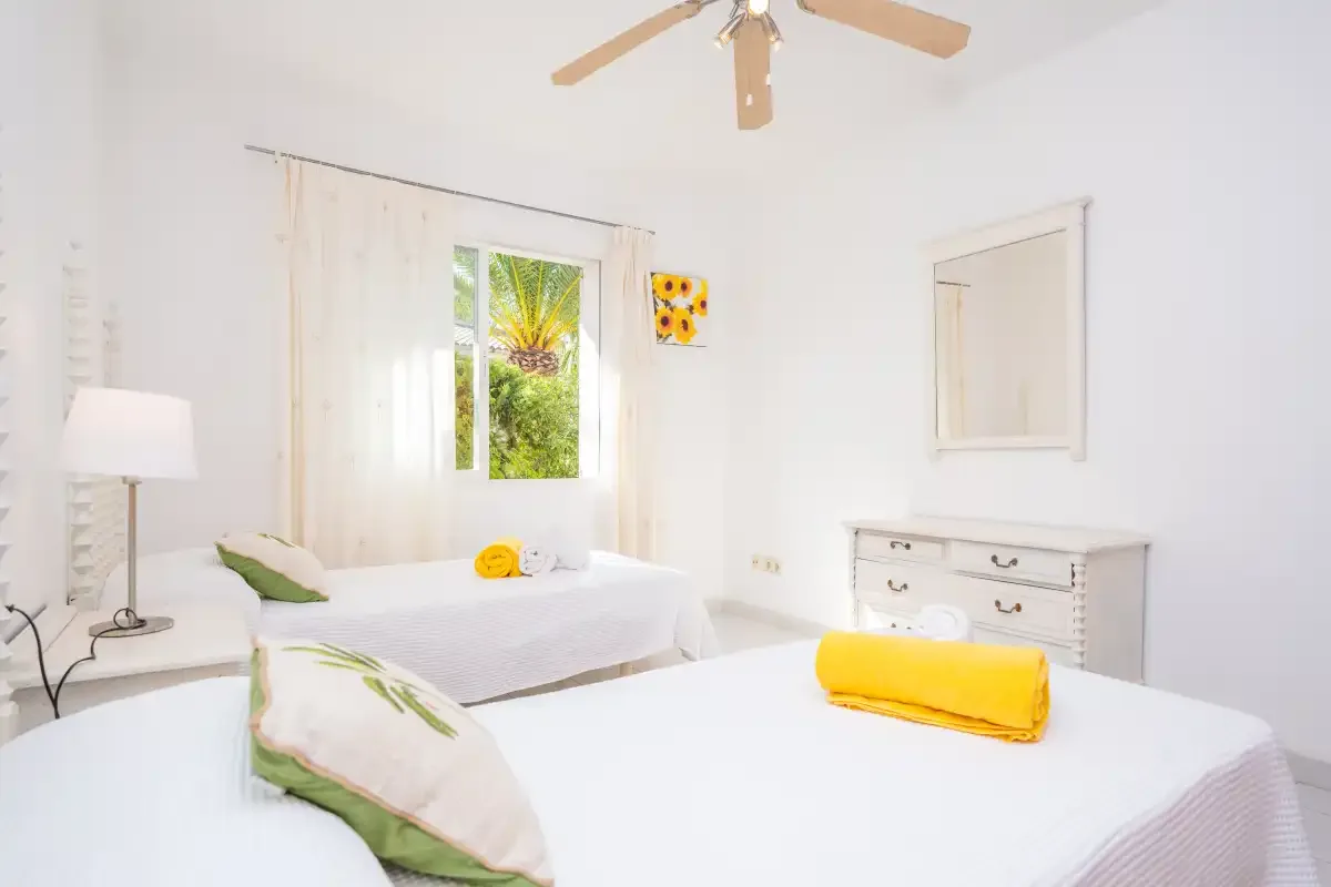 A bright bedroom with white bedding and a window overlooking greenery.