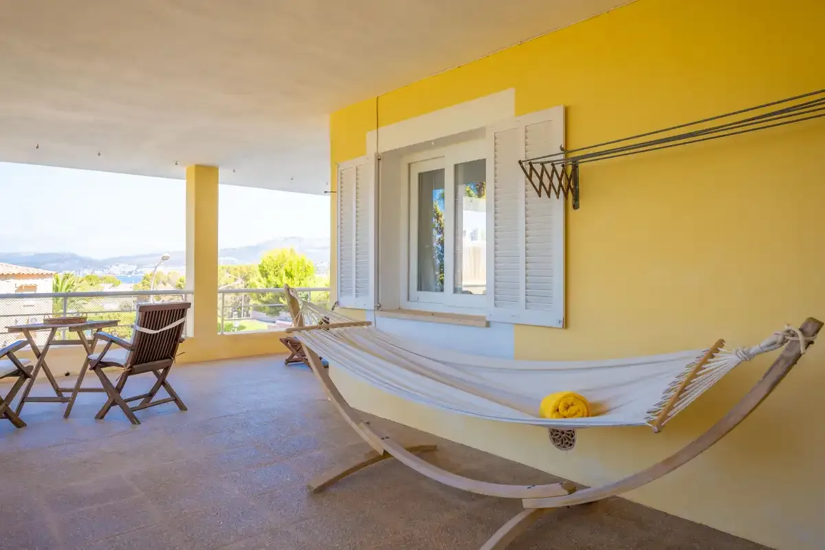 A covered terrace with a hammock, outdoor seating, and a view beyond the railing.