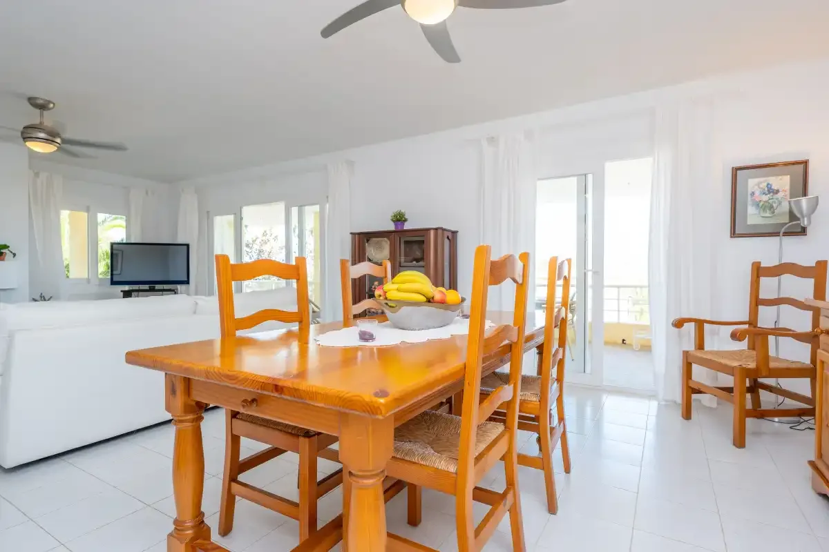 A bright dining area with wooden seating beside a living room and large windows.