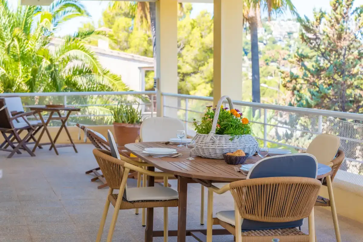 A covered outdoor dining area with a wooden table and chairs overlooks leafy gardens.