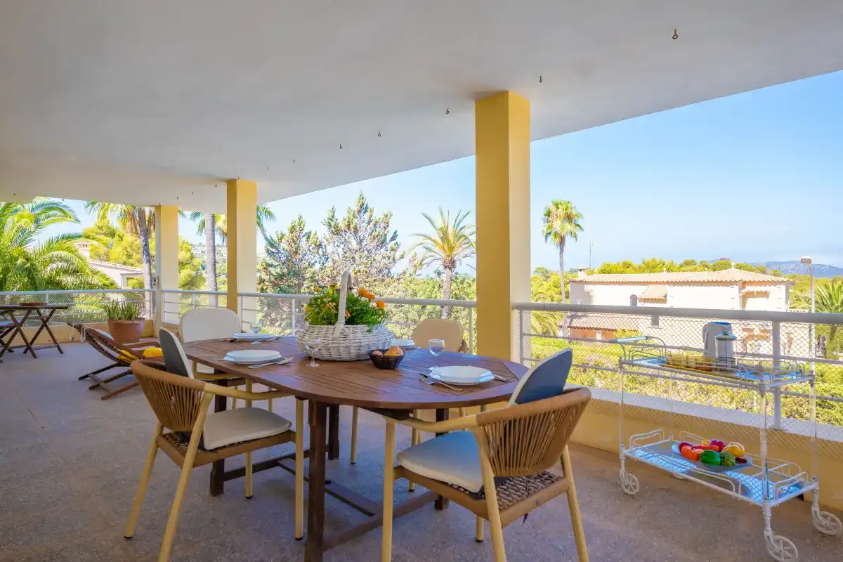 A covered outdoor dining area with a long table and chairs overlooks palm trees.