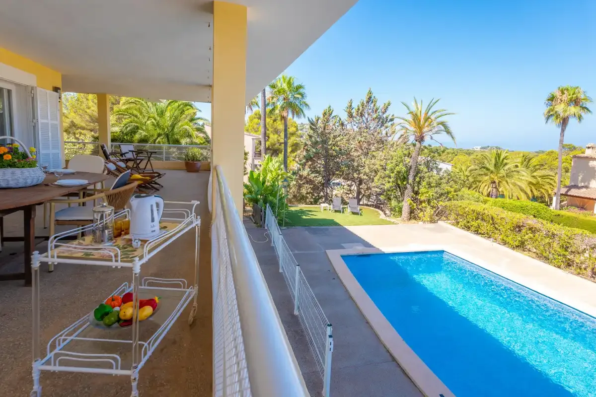 A covered outdoor dining area overlooks a swimming pool and landscaped garden.