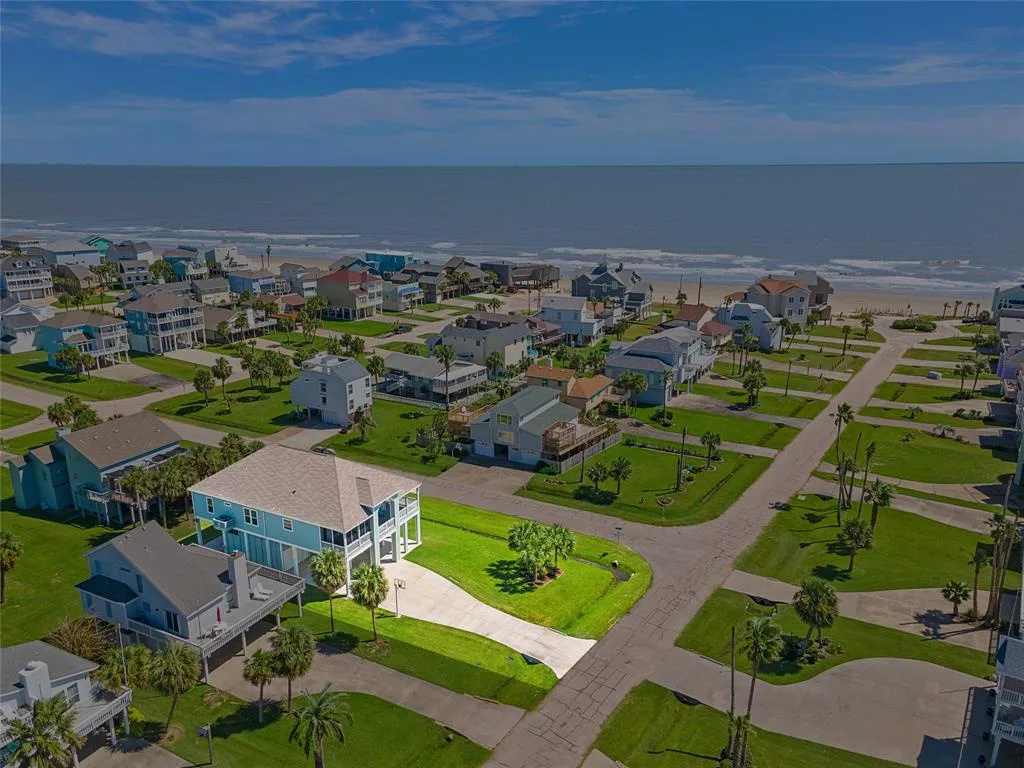Aerial view of a coastal neighborhood with homes, roads, and the ocean beyond.