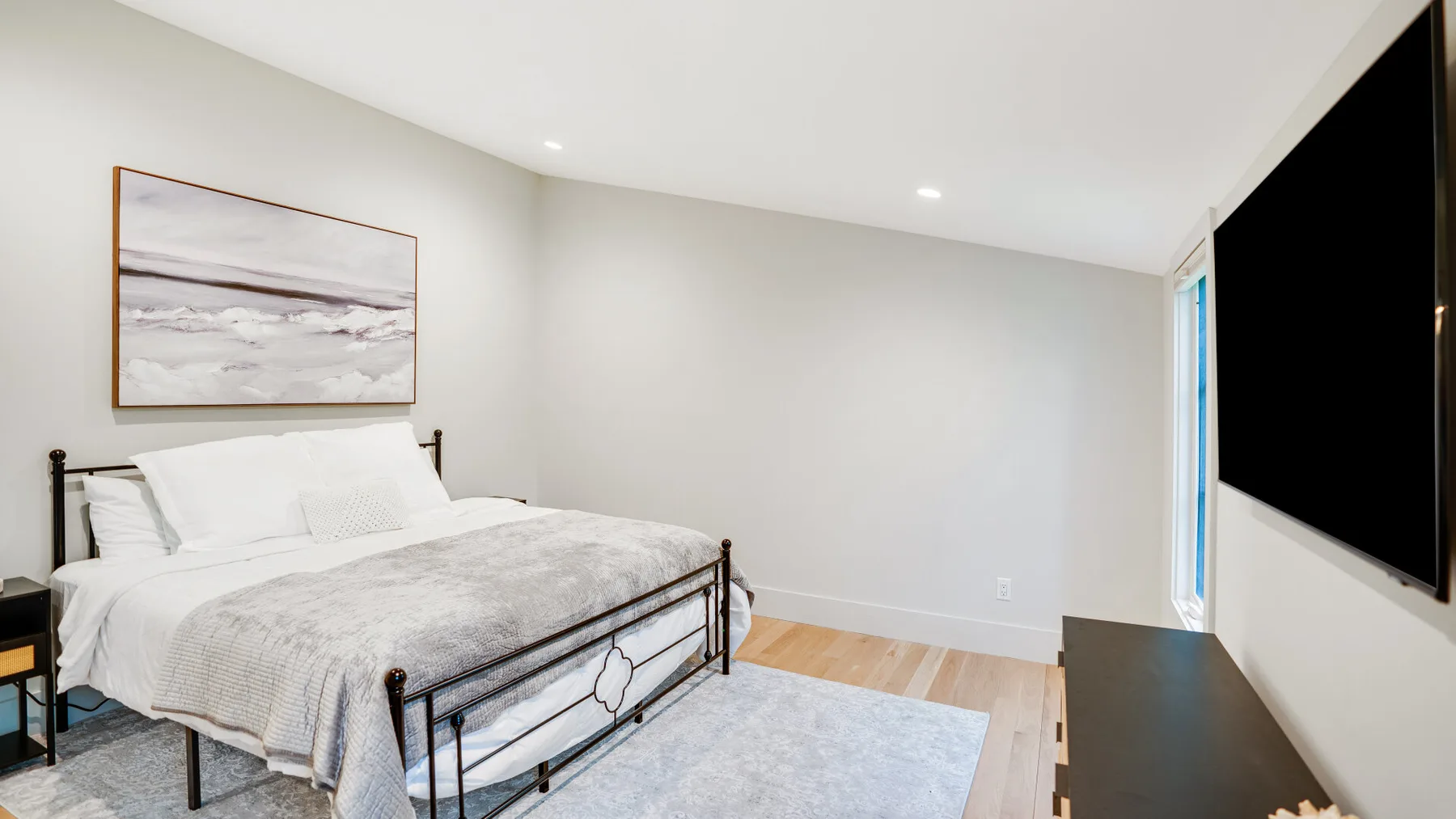 A bright bedroom with a bed, framed artwork, and a wall-mounted television.