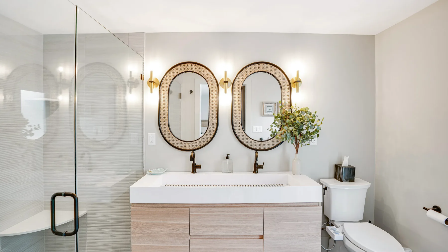 A bright bathroom with a double sink vanity, mirrors, and a glass shower.