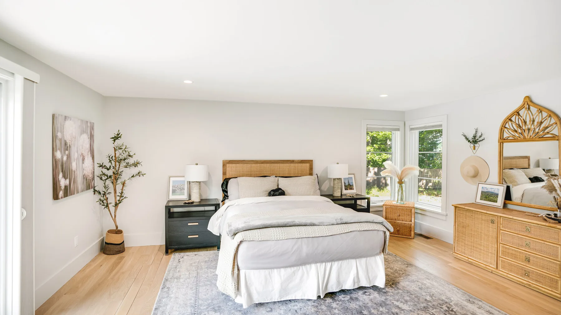 A bright bedroom with a bed, bedside tables, and a large window.