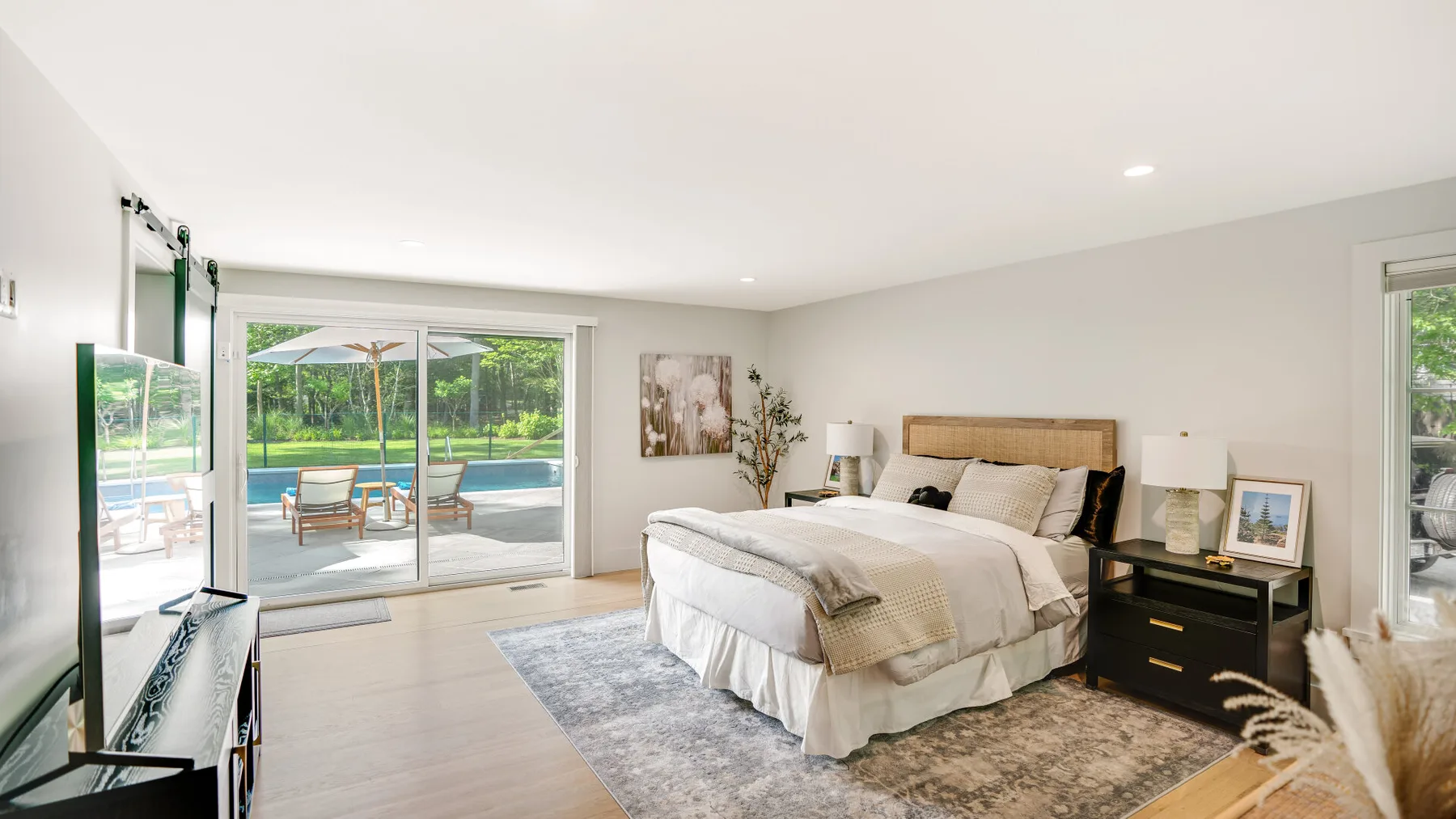 A bright bedroom with a large bed beside sliding glass doors overlooking a pool.