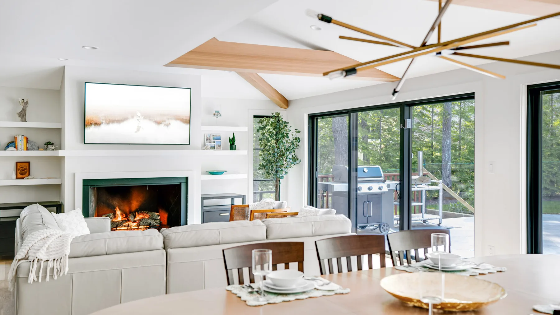 A bright living room with a fireplace, seating, and large glass doors opening onto greenery.