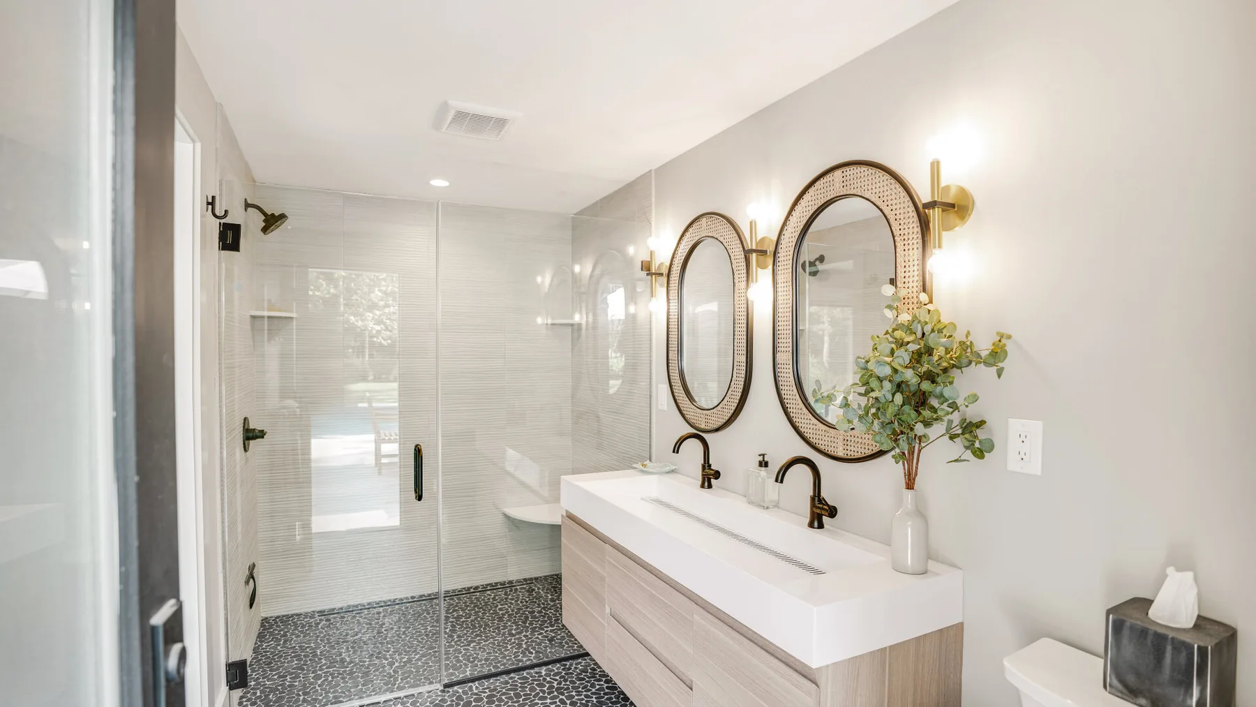 A bright bathroom with a glass shower and a long double vanity.