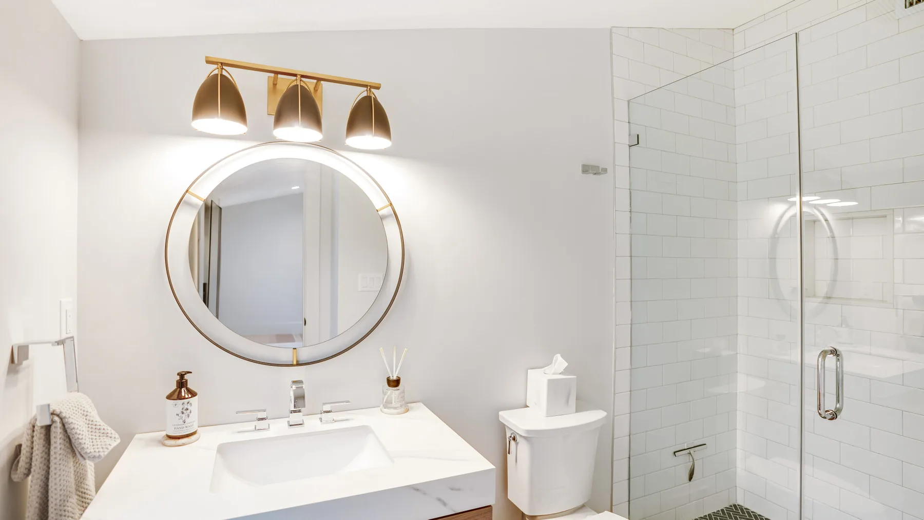 A bright bathroom with a round mirror above the sink and a glass shower.