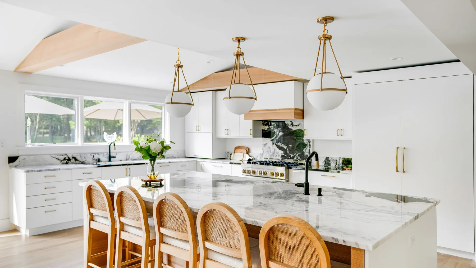 A bright kitchen with white cabinetry, marble countertops, and a row of bar stools.