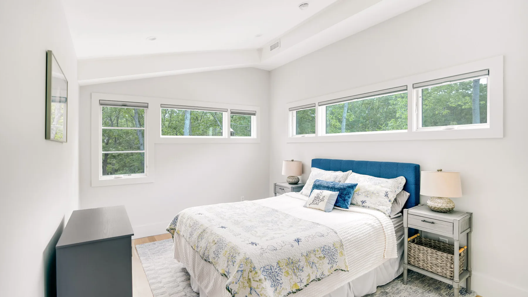 A bright bedroom with a neatly made bed beneath several windows.