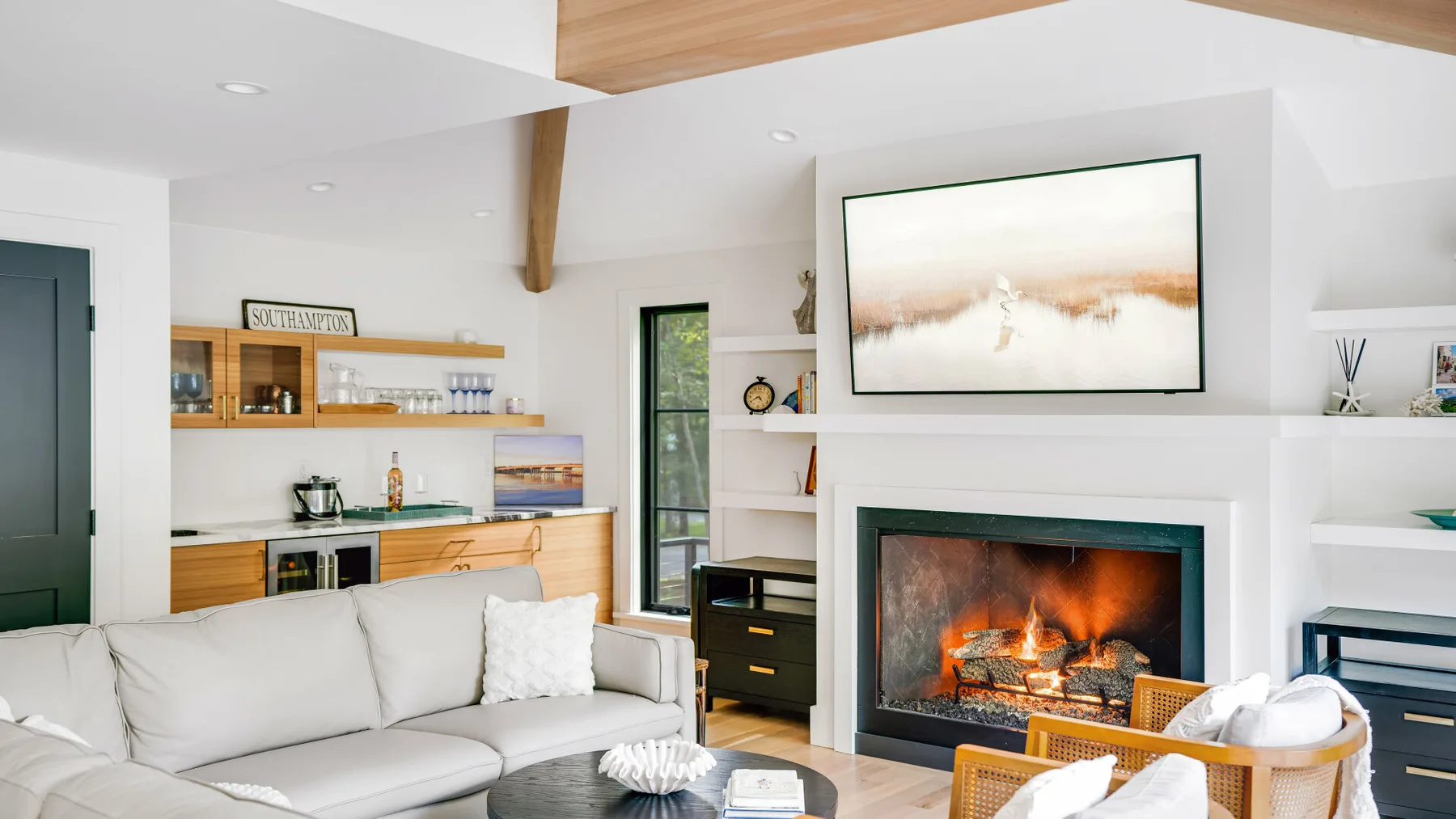 A bright living room with seating, a fireplace, and open kitchen shelving.