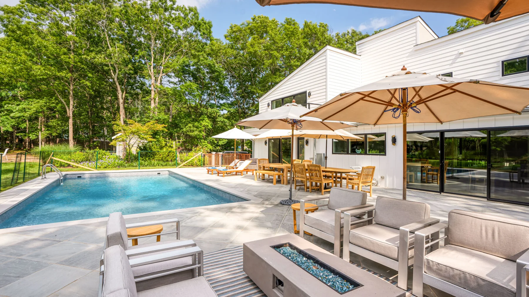 An outdoor pool beside a white building, with patio seating and umbrellas.