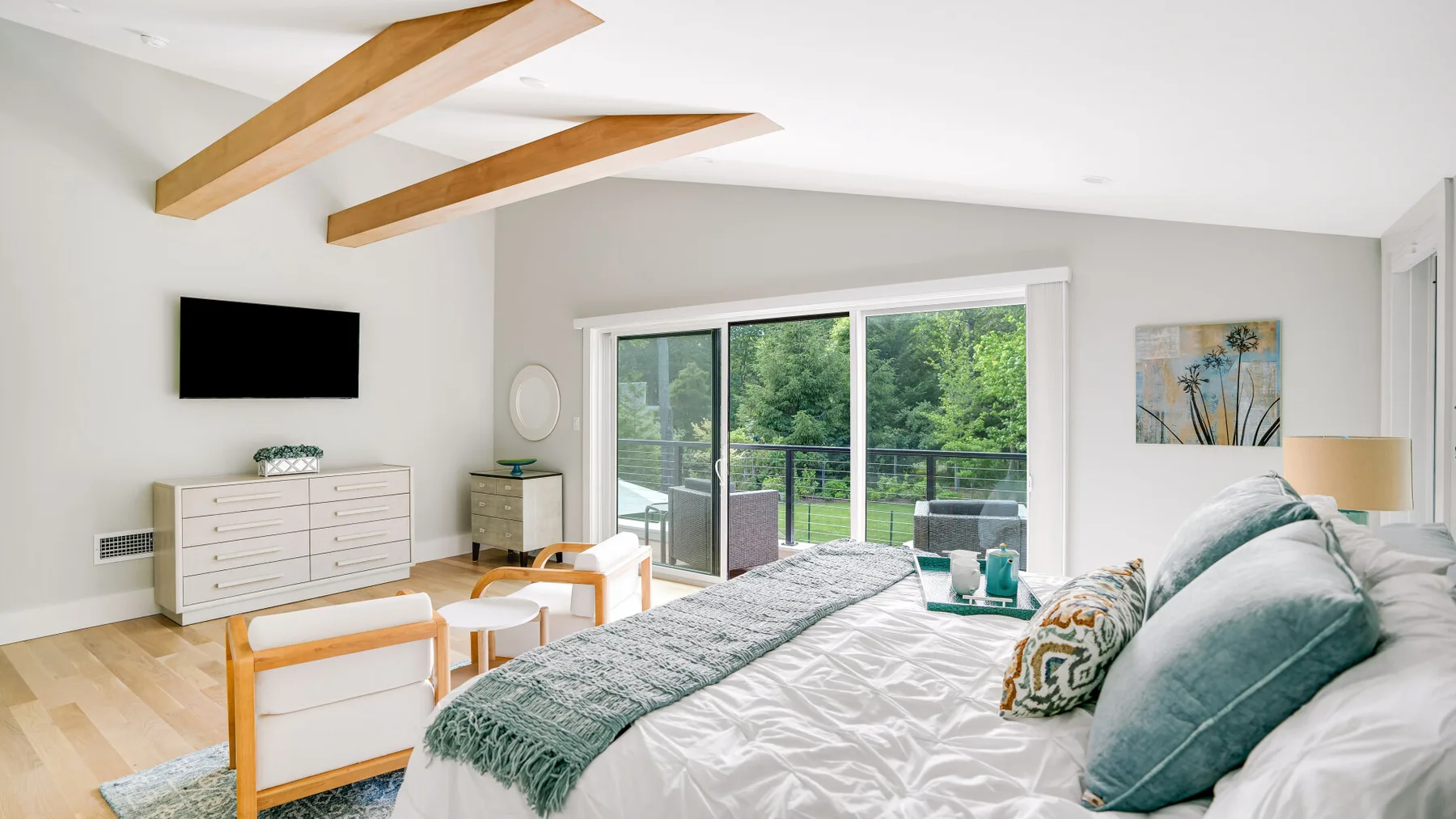 A bright bedroom with a large bed facing glass doors that open onto greenery.
