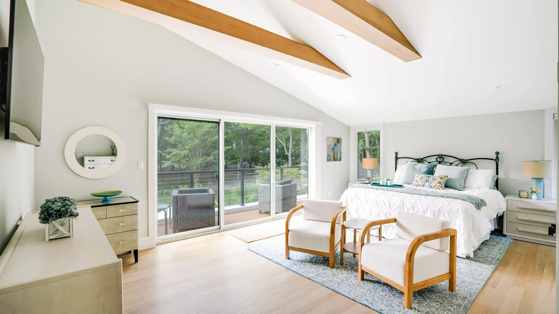A bright bedroom with a large bed, two chairs, and sliding glass doors.