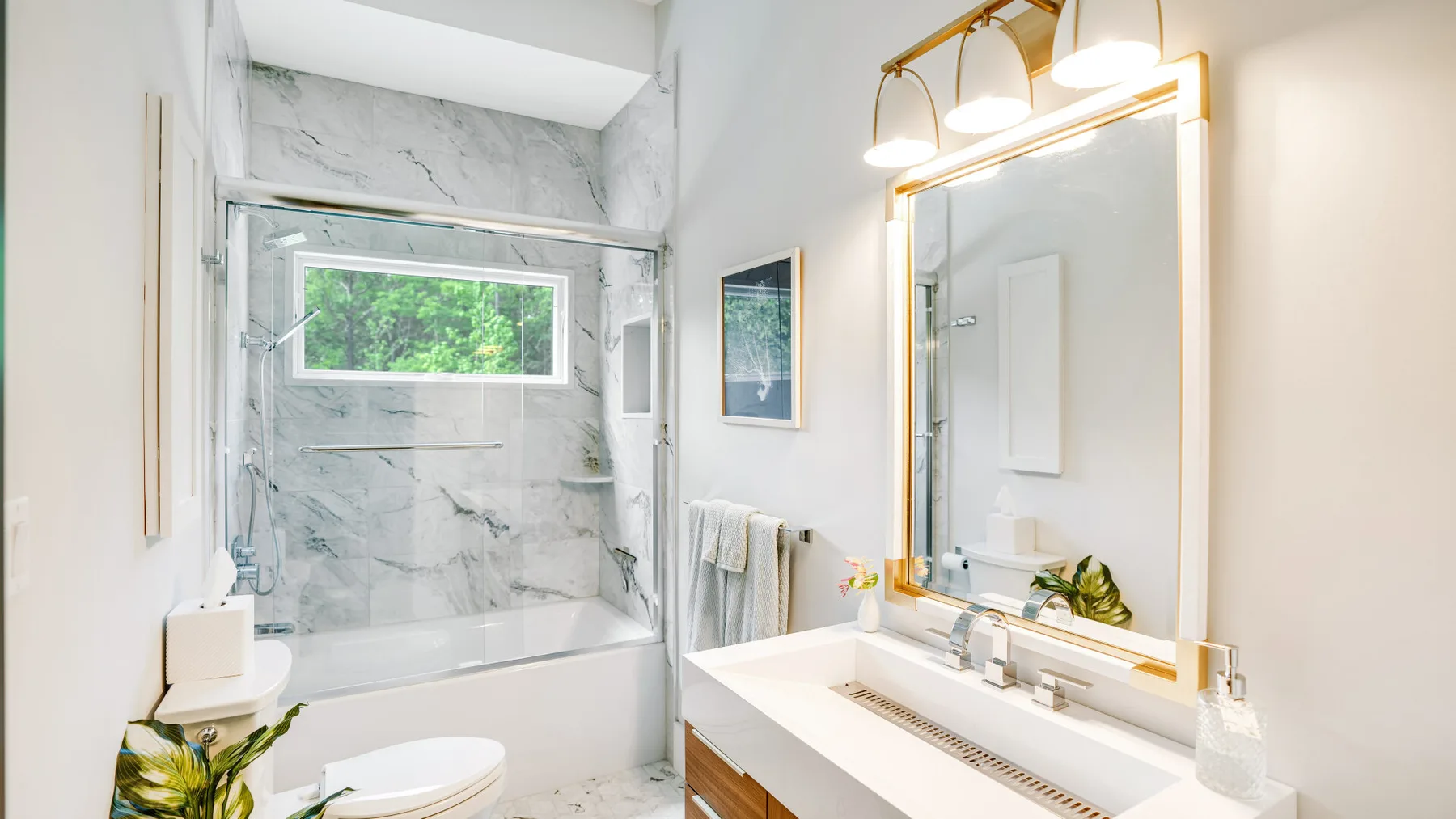 A bright bathroom with a bathtub, glass shower panel, and wide vanity.