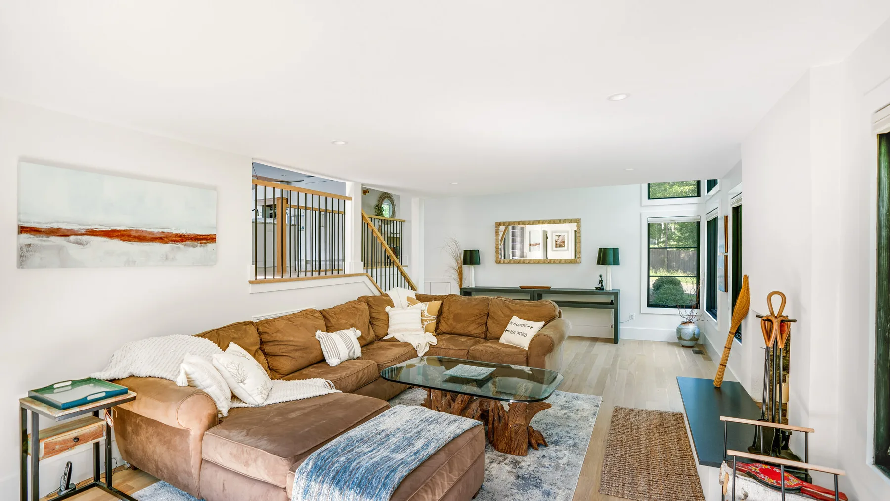 A bright living room with sectional seating, a glass coffee table, and large windows.