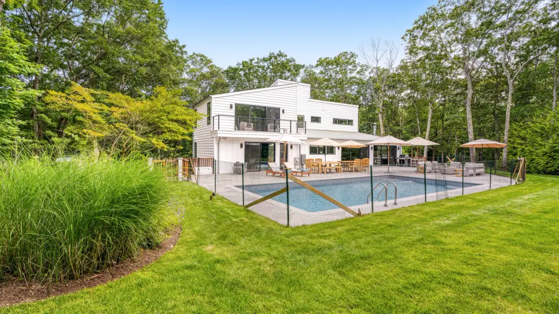 A modern house overlooks a swimming pool and a broad green lawn.