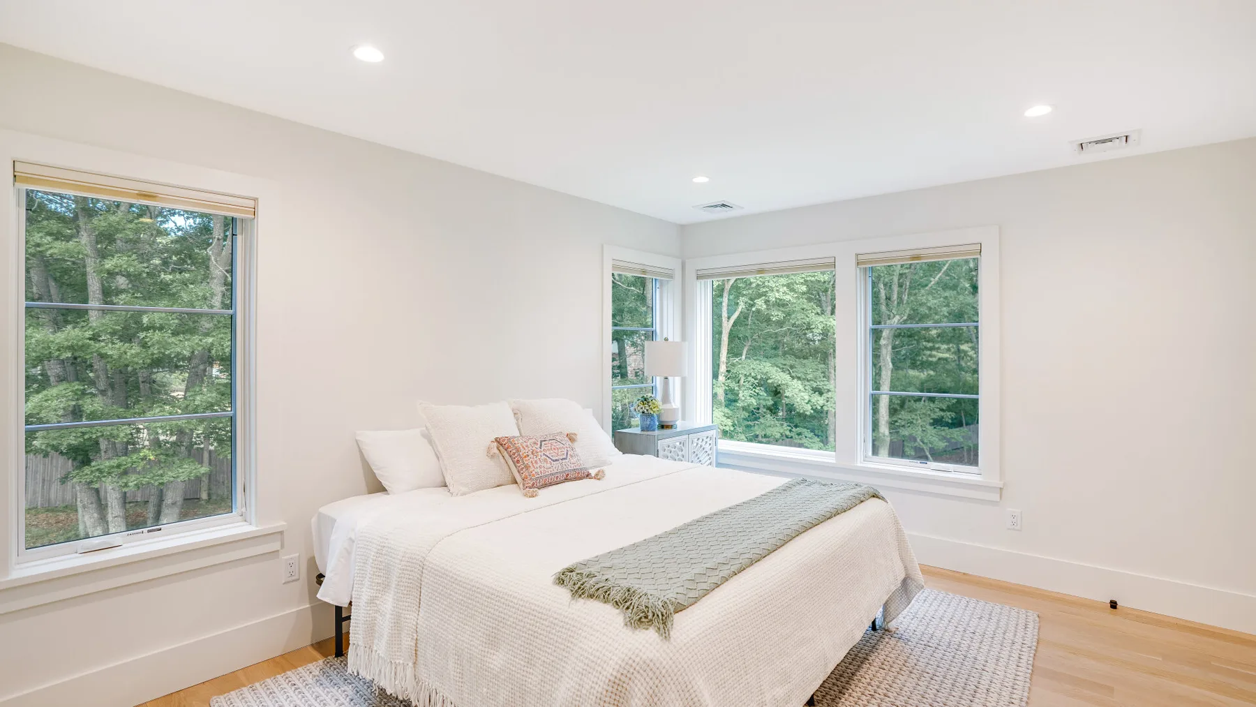 A bright bedroom with a bed and large windows overlooking trees.