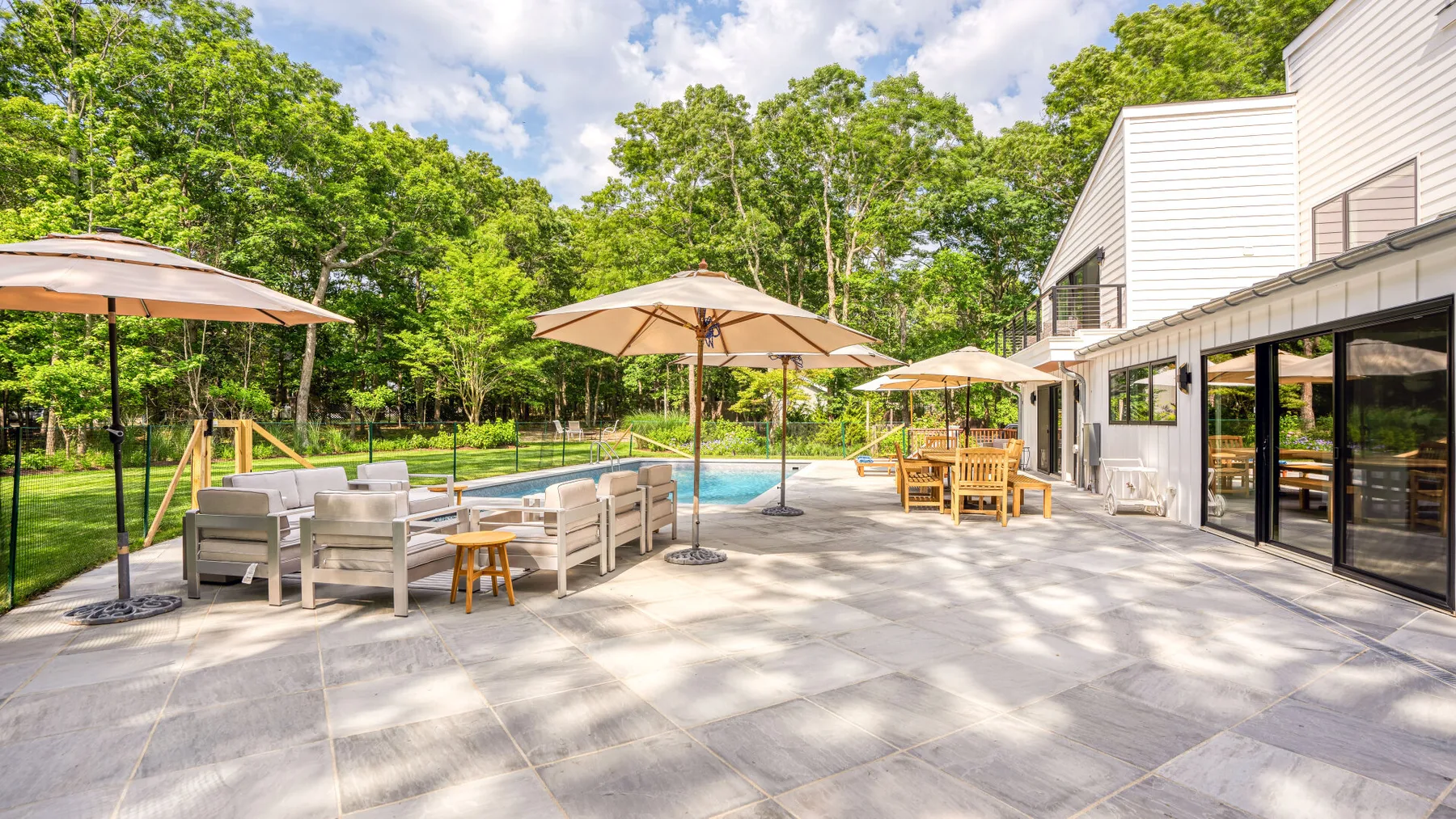 An outdoor patio with seating and umbrellas beside a swimming pool.