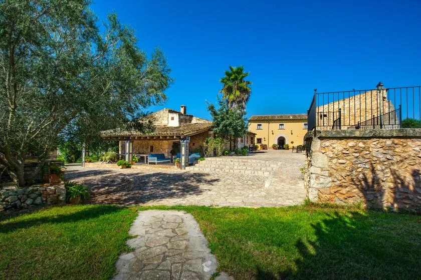 Un sendero de piedra atraviesa un jardín y conduce a un patio soleado y un edificio.