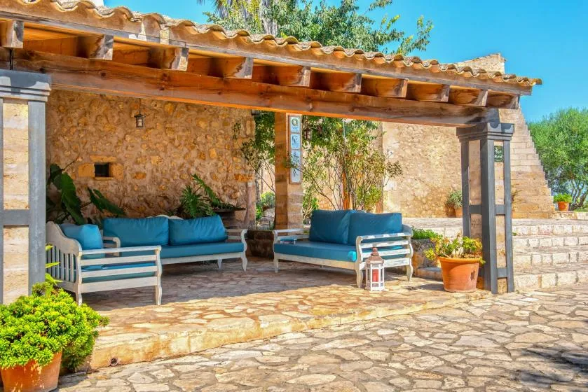 Una zona de estar exterior a la sombra, con cojines azules bajo una pérgola de madera.