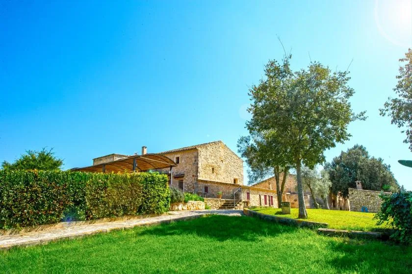 Una casa de piedra está junto a un césped verde, árboles y un seto.