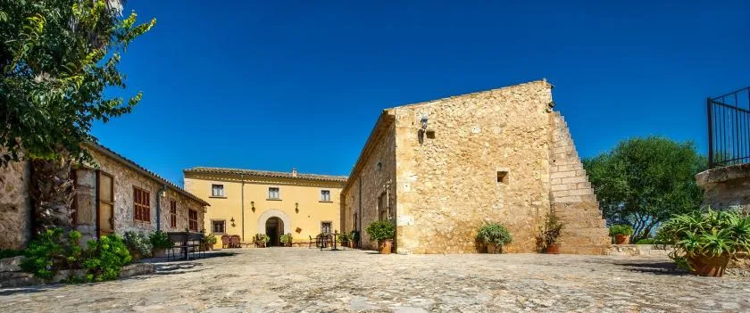 Un patio de piedra soleado, rodeado de edificios de aspecto histórico y plantas.