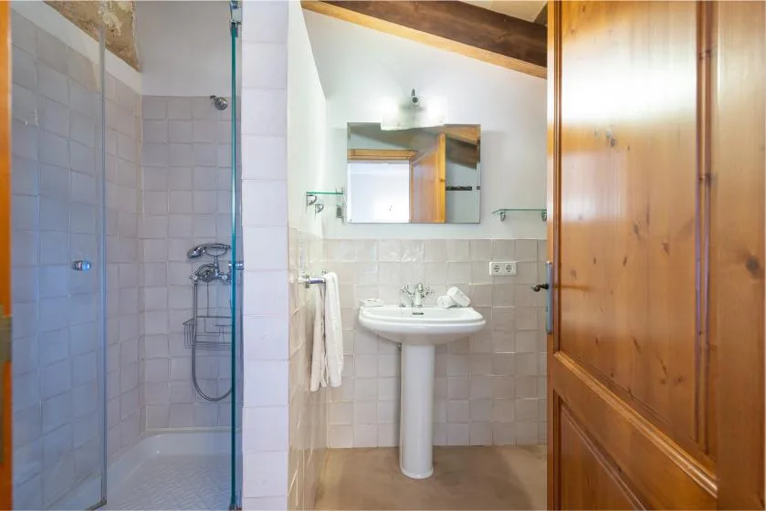 Un baño alicatado con ducha de vidrio, lavabo y puerta de madera.