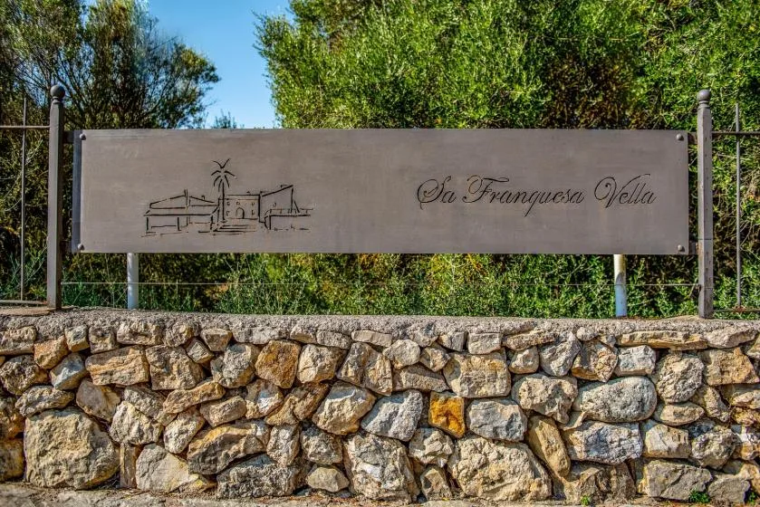 Un letrero de una villa está sobre un muro de piedra, con árboles detrás.