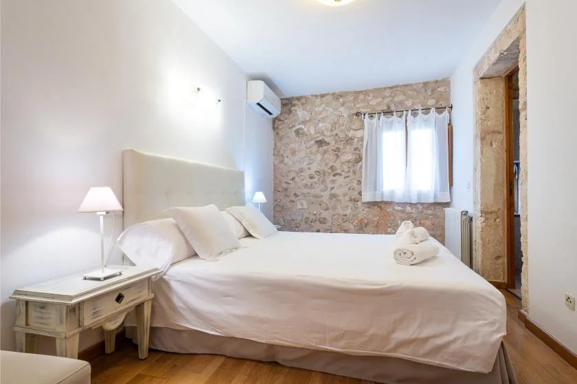 Un dormitorio con una cama grande, una mesita de noche y una ventana con cortinas translúcidas.