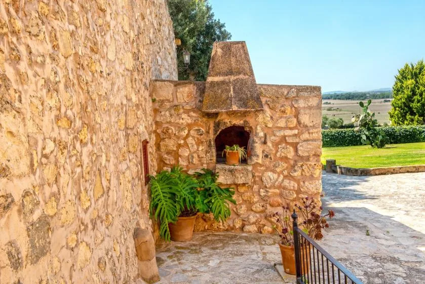 Una chimenea exterior de piedra está junto a un patio pavimentado con vistas a campos verdes.