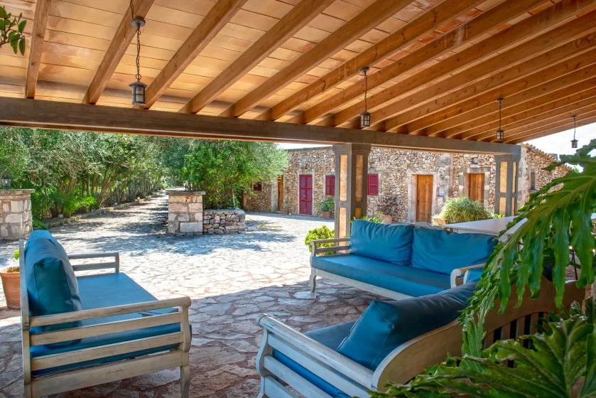 Una zona de estar al aire libre cubierta da a un patio de piedra y un jardín frondoso.