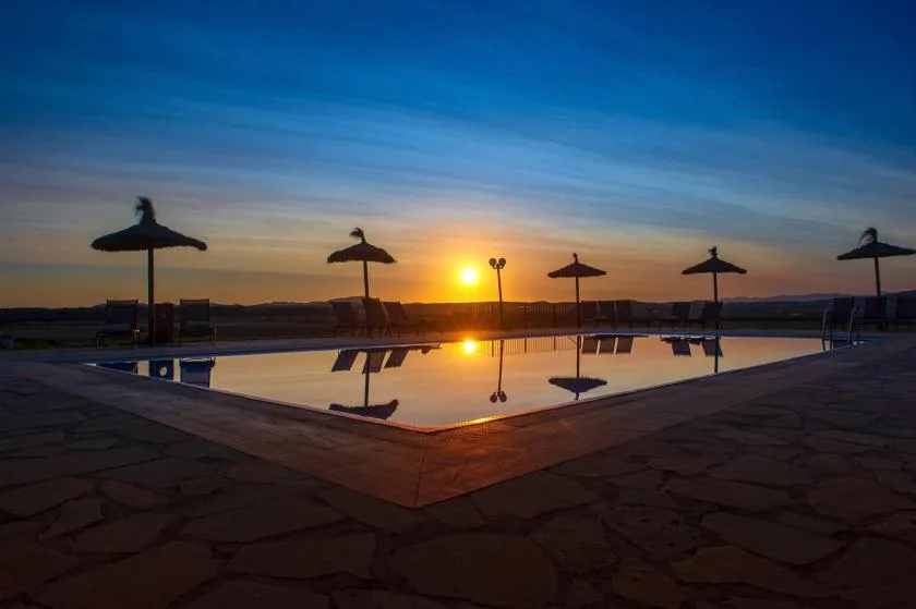 Una piscina refleja el atardecer, con sombrillas junto al borde opuesto.