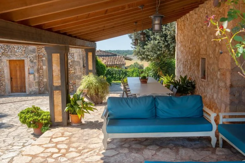 Un patio cubierto de piedra con asientos azules y una mesa de comedor rodeada de plantas.