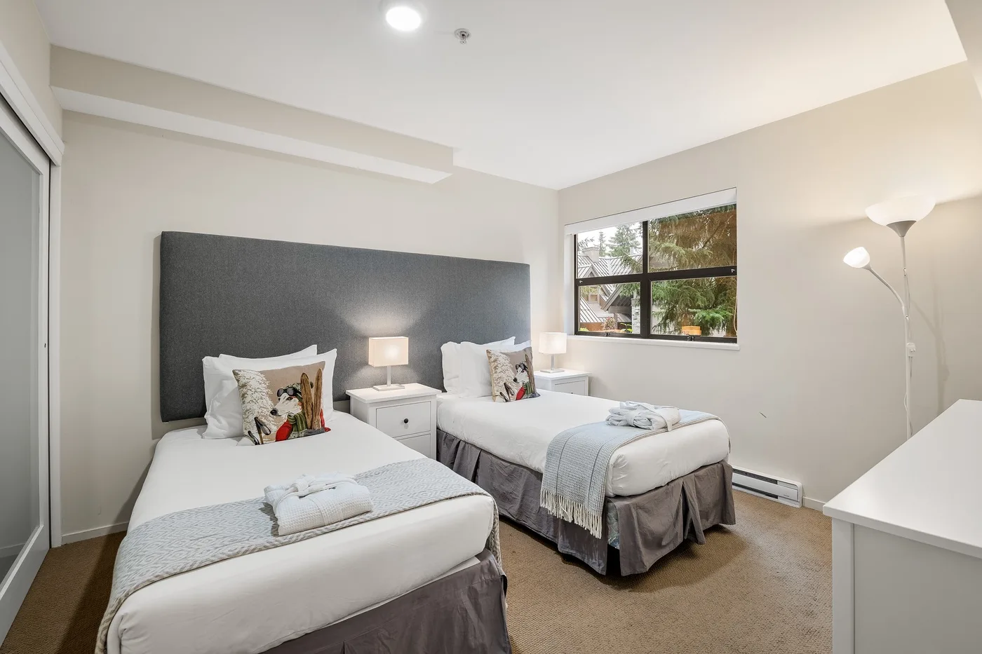 Un dormitorio luminoso con dos camas, mesitas de noche y una ventana.