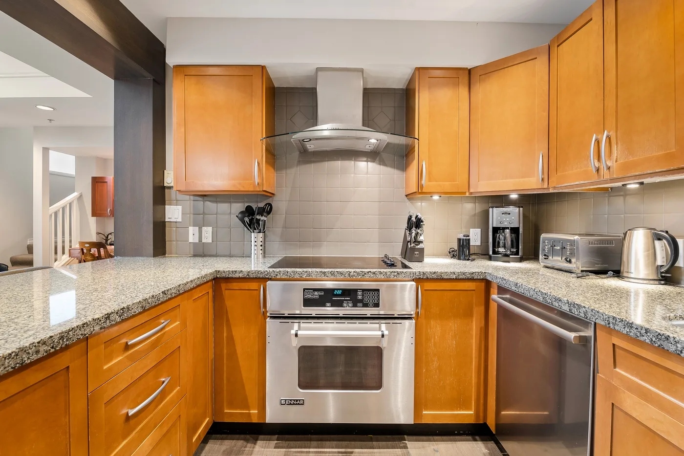 Una cocina con gabinetes de madera, encimeras de granito y electrodomésticos de acero inoxidable.