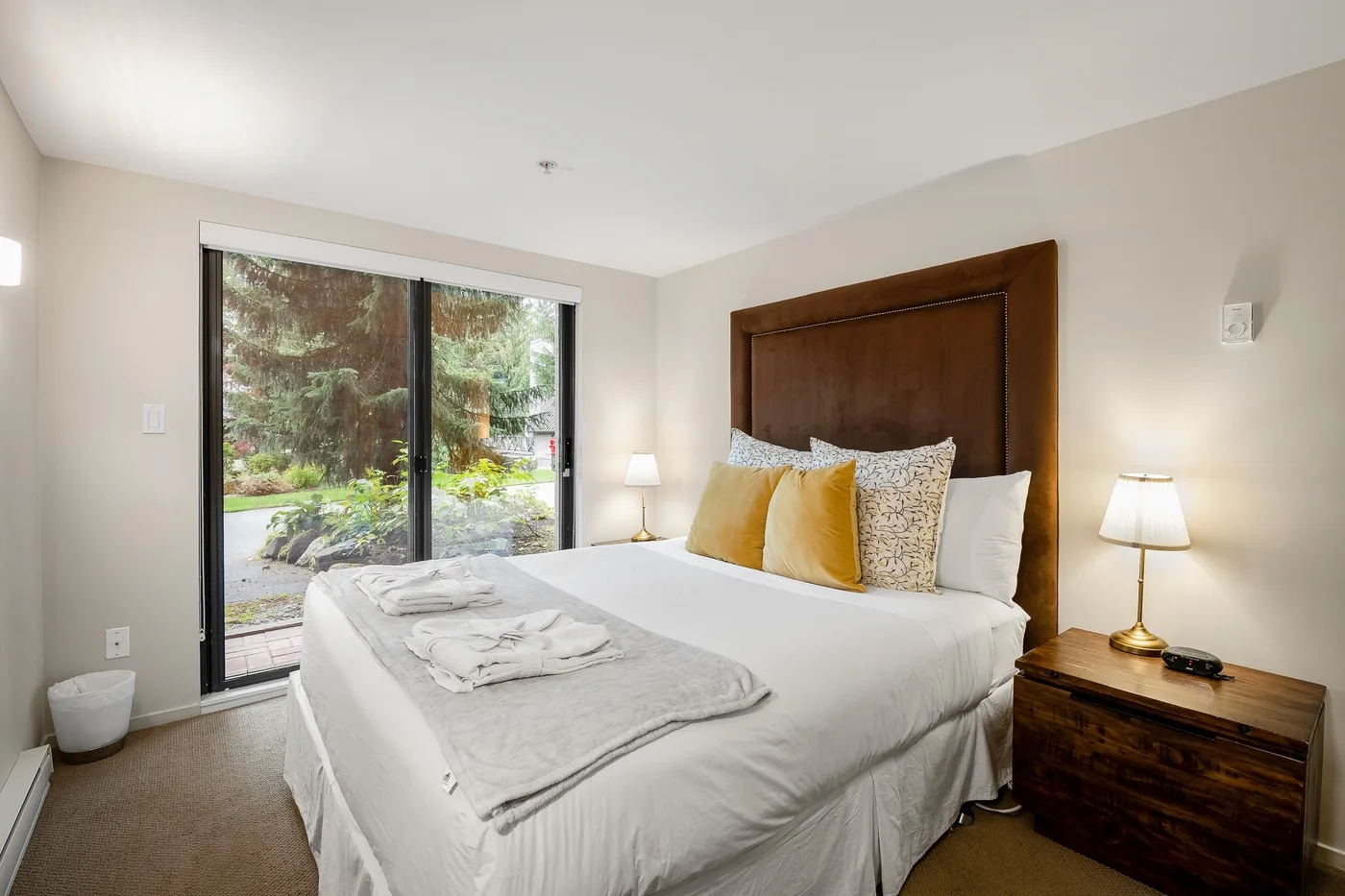 Un dormitorio con una cama bien tendida y una ventana grande con vistas a vegetación.
