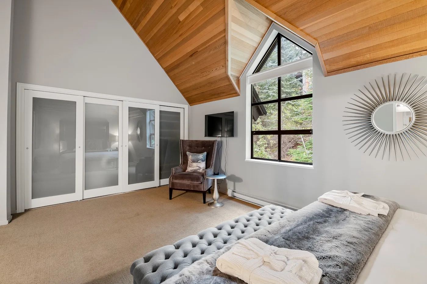 Un dormitorio con techo abovedado de madera, ventanas grandes y una cama.