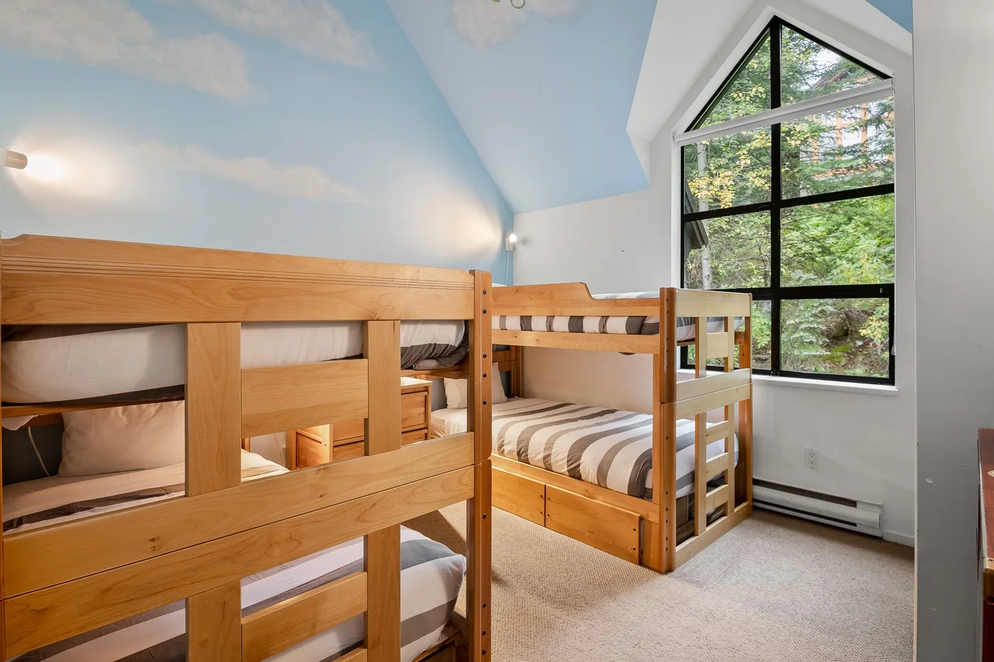 Un dormitorio con literas de madera y una gran ventana con vistas a los árboles.