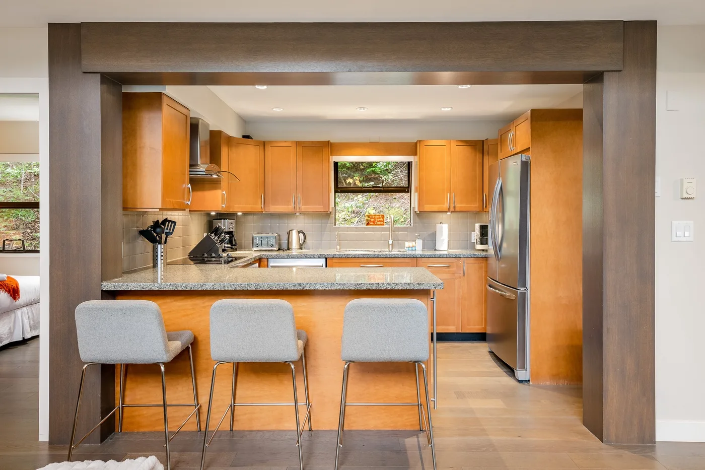 Una cocina abierta con gabinetes de madera, una isla central y tres taburetes.