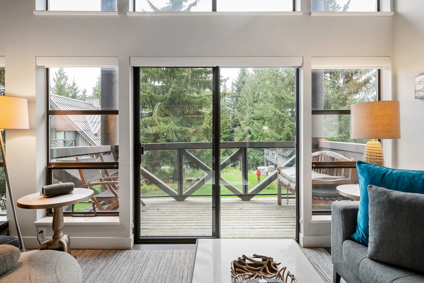 Una sala luminosa da a una terraza de madera a través de grandes puertas de vidrio.