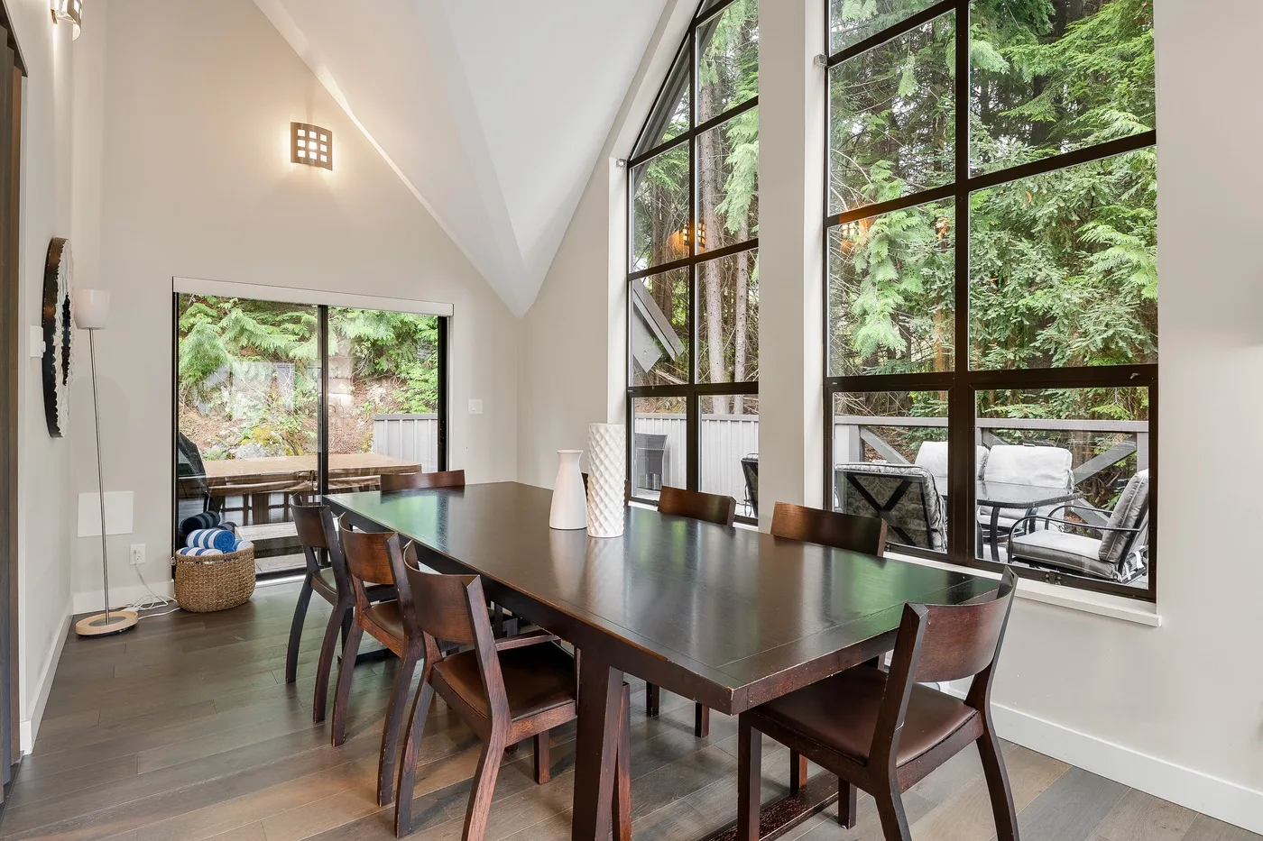 Un comedor con una mesa larga y grandes ventanas con vistas a la vegetación.