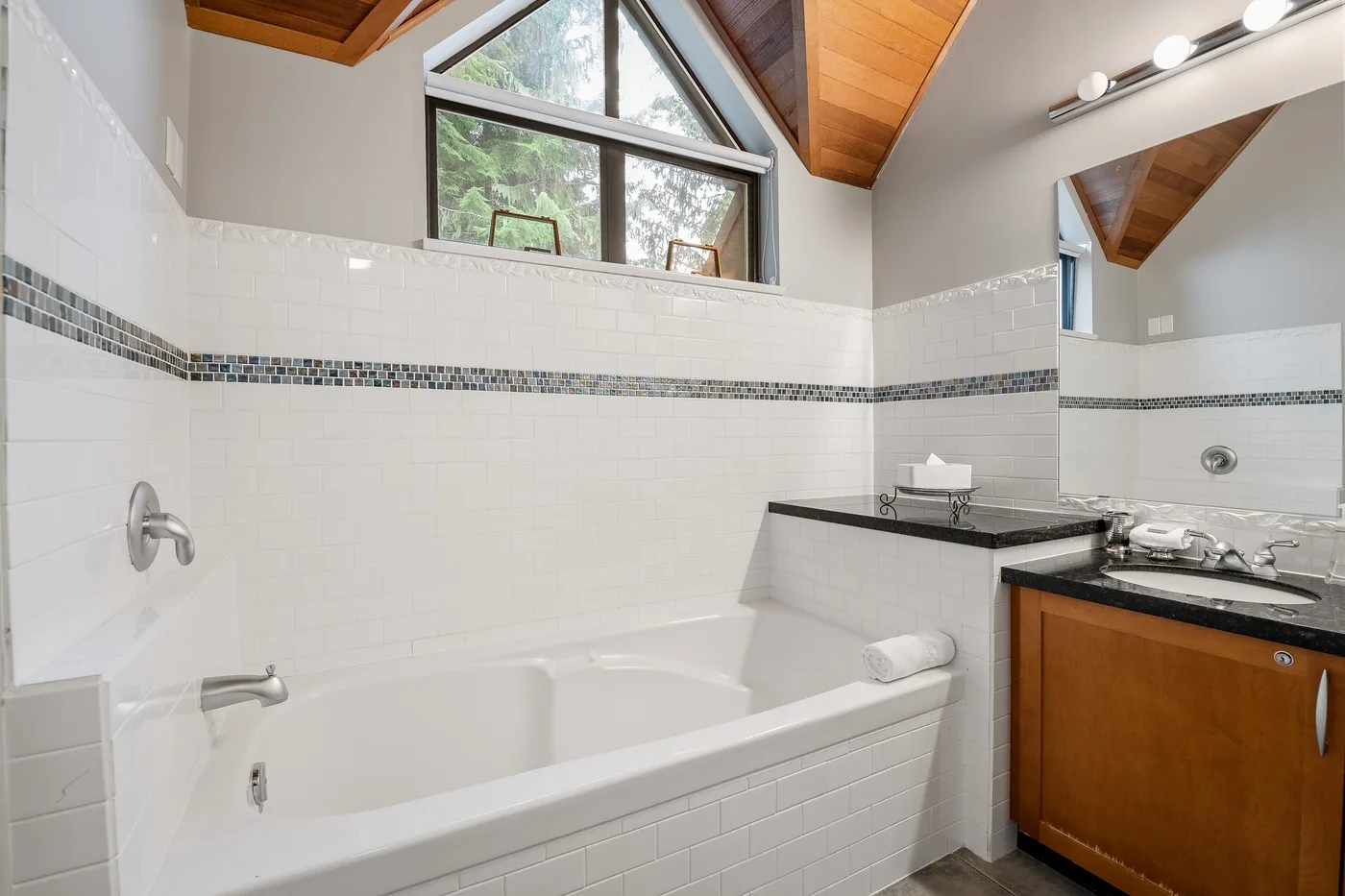 Un baño alicatado con bañera, lavabo y una ventana alta.