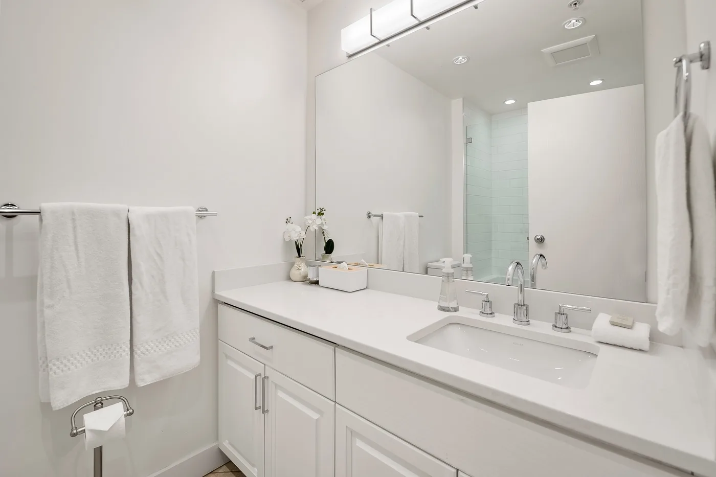 Un tocador de baño luminoso con un espejo amplio y toallas blancas.