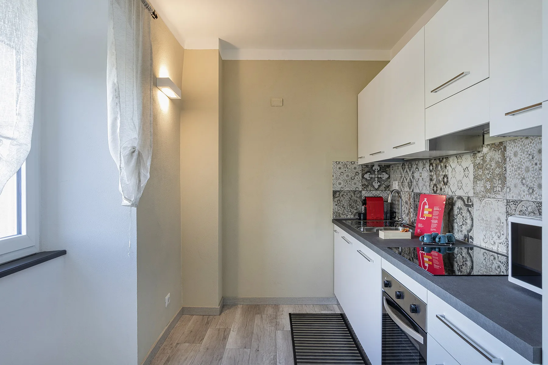 A narrow kitchen with white cabinets, dark counters, and a patterned backsplash.